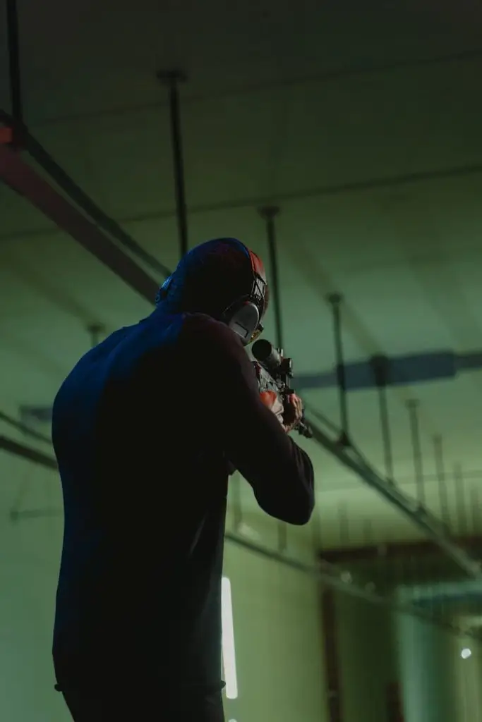 Man in black sweater aiming rifle indoors with focus on target practice.