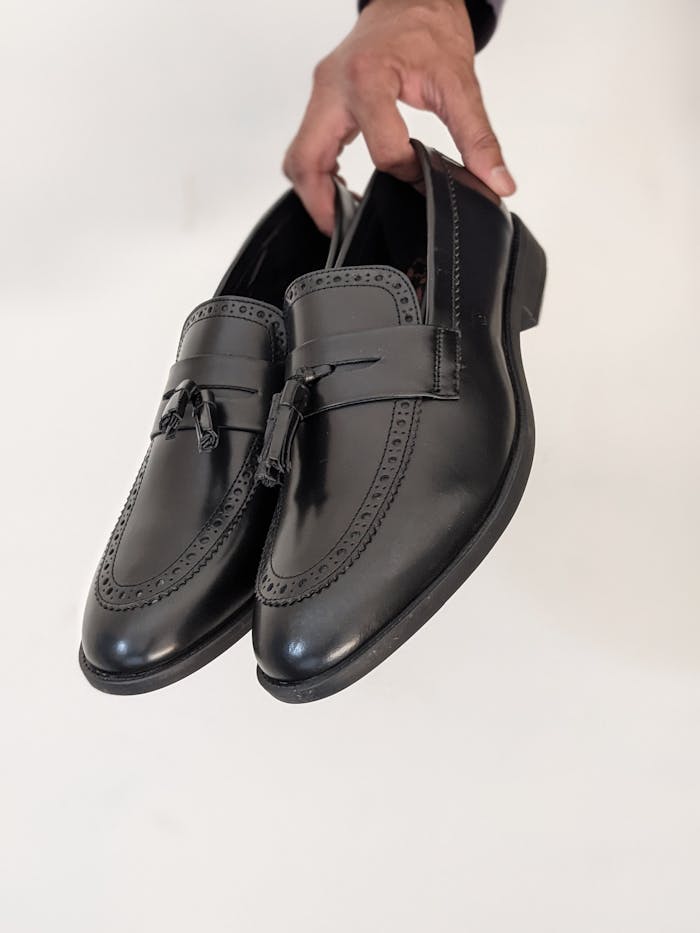 Stylish black leather dress shoes being held, perfect for fashion and lifestyle themes.