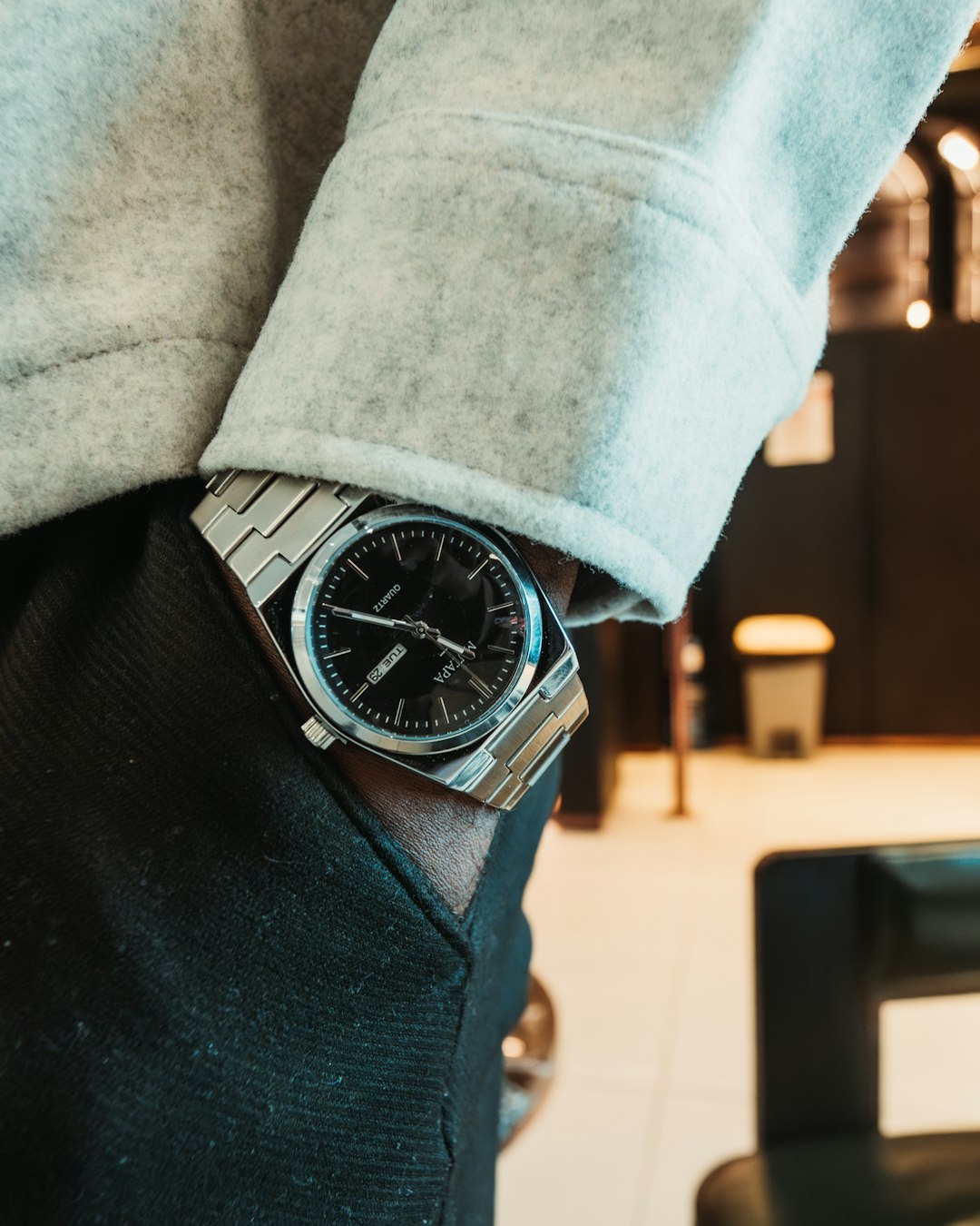 A close up shot of a man wearing a stainless steel wristwatch, captured in soft natural lighting.