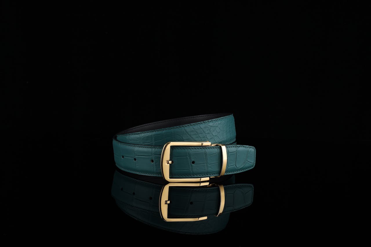 Luxurious crocodile embossed leather belt with a sleek golden buckle against a black background.
